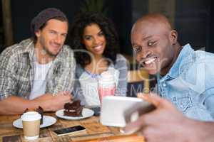 Friends taking selfie at wooden table in coffee shop