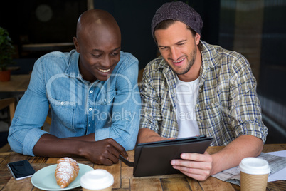 Happy male friends using digital tablet in coffee house