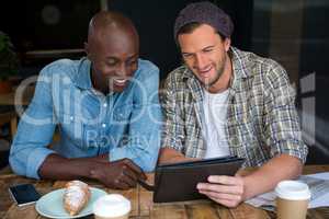 Happy male friends using digital tablet in coffee house