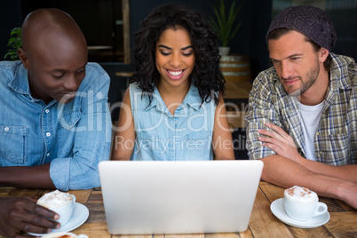 Smiling friends using laptop at table in coffee house