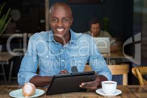 Happy young man using tablet computer at table in coffee shop