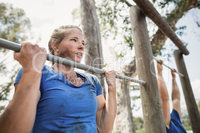 Fit man and woman performing pull-ups on bar during obstacle course