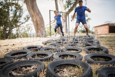 Man and woman running over the tyre during obstacle course