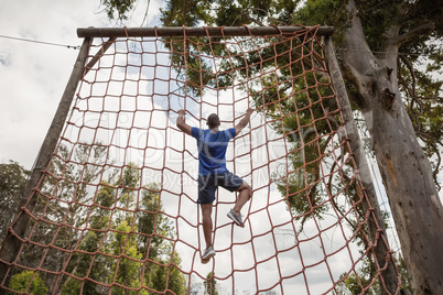 Fit man climbing a net during obstacle course