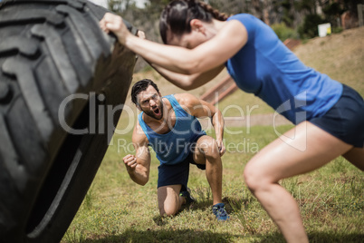 Fit woman flipping a tire while trainer cheering during obstacle course