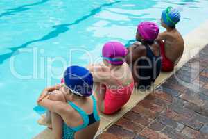 Rear view of swimmers sitting at poolside