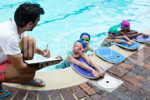 Instructor writing on clipboard with swimmers at poolside