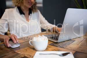 Woman using laptop with coffee on table in cafe