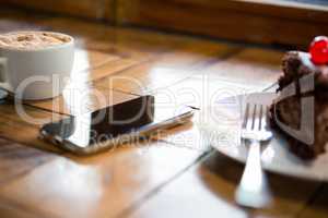 Smart phone with pastry and coffee cup on table