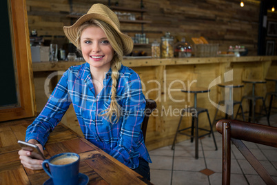 Portrait of woman wearing hat while holding mobile phone in coffee shop