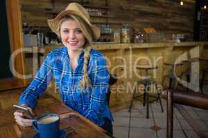 Portrait of woman wearing hat while holding mobile phone in coffee shop