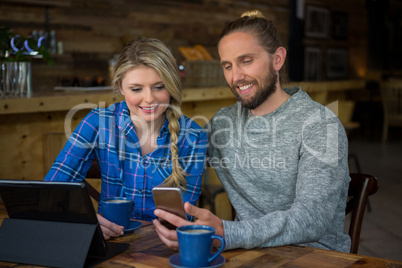 Smiling couple using cellphone at table in cafe