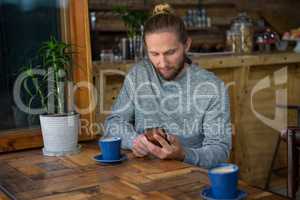 Male hipster using mobile phone at table in coffee shop