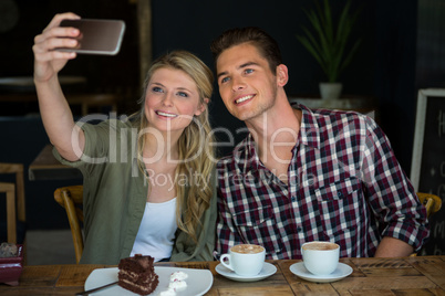 Smiling couple taking selfie with cell phone in cafeteria