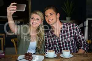 Smiling couple taking selfie with cell phone in cafeteria