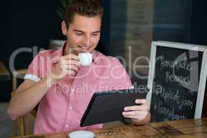 Man having coffee while using digital tablet in cafe