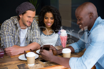 Man showing mobile phone to friends at table in coffee shop