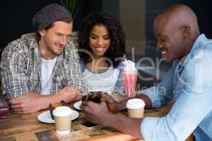 Man showing mobile phone to friends at table in coffee shop