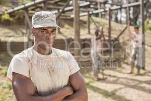 Military man standing with arms crossed during obstacle course in boot camp