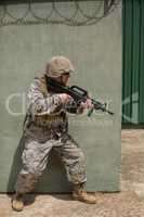 Military soldier aiming with a rifle against concrete wall