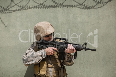 Military soldier aiming with a rifle against concrete wall