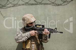 Military soldier aiming with a rifle against concrete wall