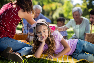 Girl resting on blanket besides family enjoying the picnic