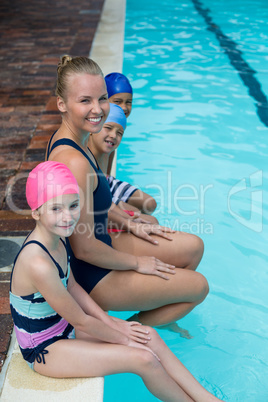 Happy swimming instructor with students sitting at poolside