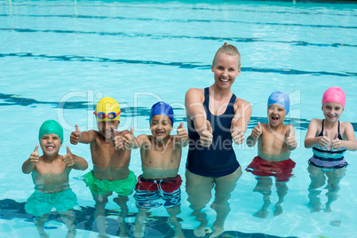 Trainer and children showing thumbs up in swimming pool