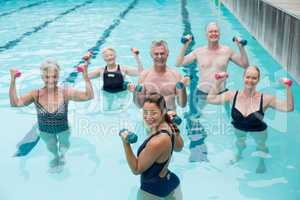 Senior swimmers and trainer lifting dumbbells in swimming pool