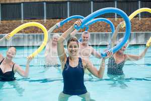 Cheerful trainer and senior swimmers exercising with pool noodle
