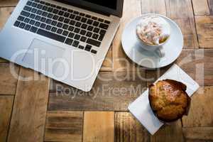 Laptop with coffee and muffin on wooden table in cafe