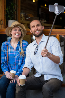 Smiling couple photographing through selfie stick in coffee shop