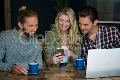 Smiling friends using smart phone at table in cafeteria