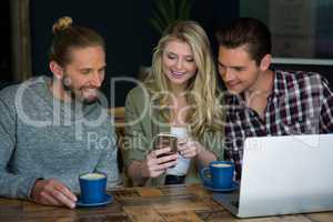 Smiling friends using smart phone at table in cafeteria