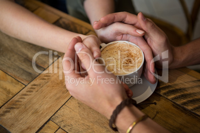 Couple holding hands and coffee cup in cafeteria