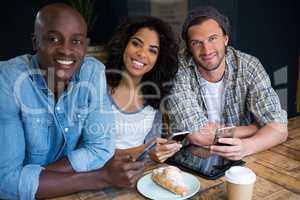 smiling friends holding smart phones at table in coffee shop