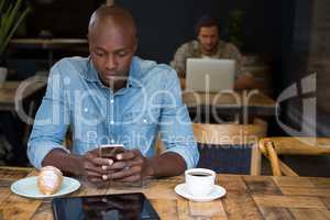 Man using mobile phone at wooden table in coffee shop