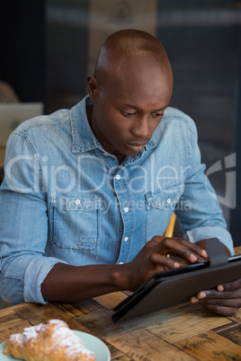 Man using digital tablet at wooden table in coffee house