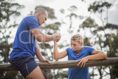 Man assisting woman to climb a hurdles during obstacle training