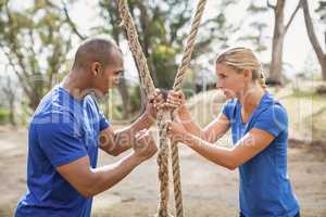 Male trainer assisting woman in rope climbing during obstacle course