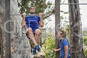 Fit man and woman performing pull-ups on bar during obstacle course