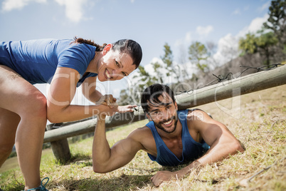 Smiling fit woman helping man crawling under the net during obstacle course