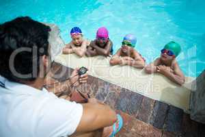 Instructor using stopwatch while training little swimmers at poolside