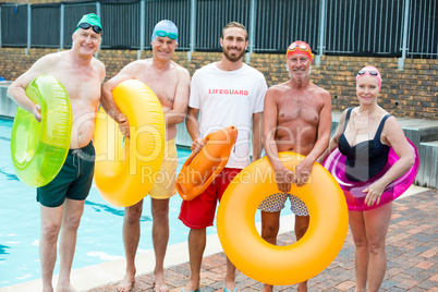 Male lifeguard with senior swimmers standing at poolside