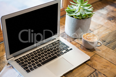 Close-up of laptop by coffee cup in cafeteria