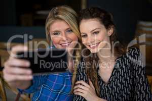 Smiling women taking selfie through smart phone in coffee shop
