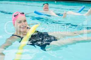 Mature couple swimming with pool noodles