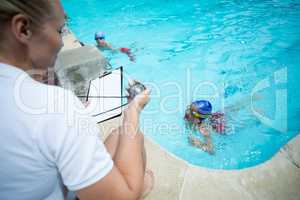 Female instructor monitoring time of children swimming in pool