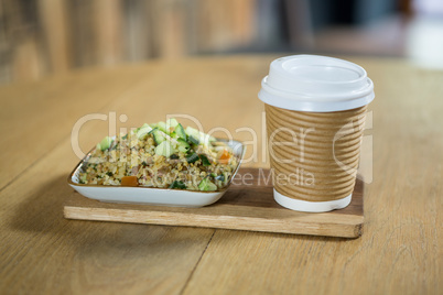 Food and disposable coffee cup on wooden table in cafe